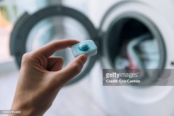 hand holding detergent capsule in front of washing machine - cleaning agent stock pictures, royalty-free photos & images