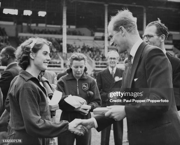 Prince Philip, Duke of Edinburgh presents English sprinter Dorothy Manley with her medal after the Great Britain women's team won the 440 yards relay...