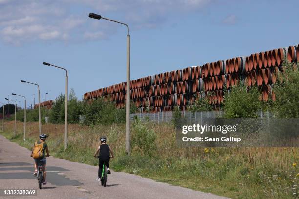 People on bicycles ride past sections of pipe for the Nord Stream 2 gas pipeline stacked at Mukran Port on Rügen Island on August 04, 2021 in...