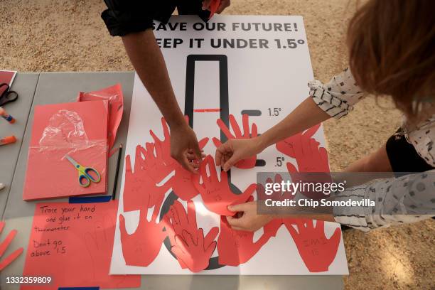 Young climate activists and their supporters paste paper handprints onto a poster during a rally on the National Mall on August 04, 2021 in...