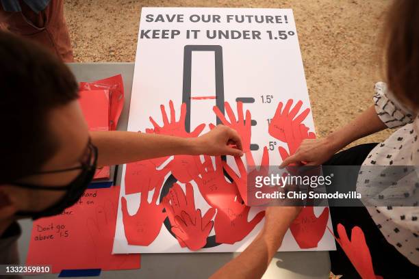 Young climate activists and their supporters paste paper handprints onto a poster during a rally on the National Mall on August 04, 2021 in...