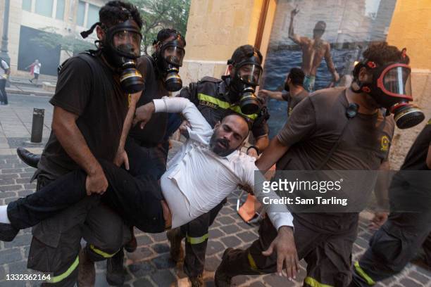 Civil defence workers help an injured protester during clashes with security forces after an anniversary commemoration of the Beirut port explosion,...