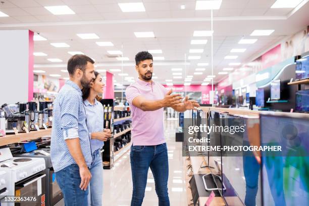 vendedor asiste a una pareja que quiere elegir el mejor televisor - salesman fotografías e imágenes de stock