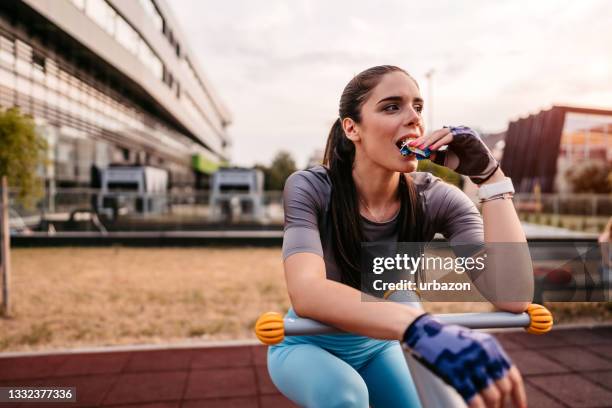 woman eating energy bar after riding bike in park - energiereep stockfoto's en -beelden
