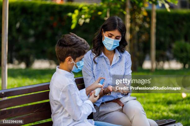 photo of young mother with little boy sitting on the bench in public park and disinfecting his hands. - antiseptic wipe stockfoto's en -beelden