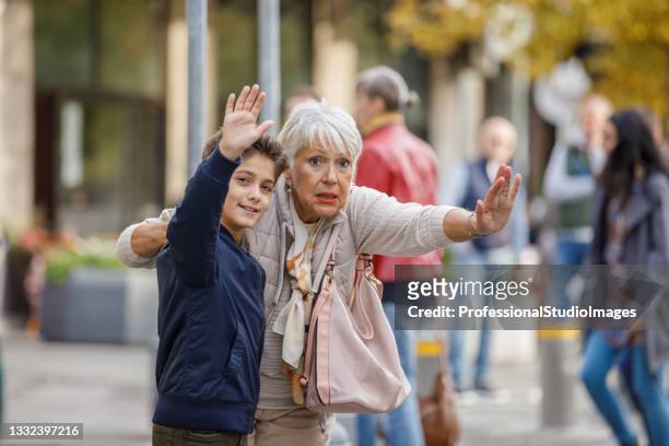 senior woman and grandson are standing near the road in city streets and trying to catch a transport. - taxi boys stock pictures, royalty-free photos & images