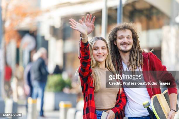 a young man and his girlfriend are standing in the street and waving with arm to catch a taxi. - female waving on street stock pictures, royalty-free photos & images