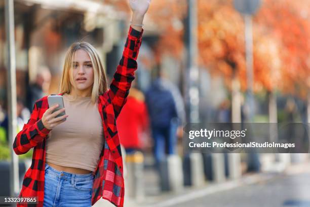 a young woman in plaid shirt is standing in the street and waving to catch a taxi. - different car models stock pictures, royalty-free photos & images