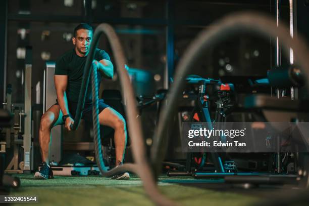 asian indian mid adult macho man practicing battle rope in gym - touw stockfoto's en -beelden