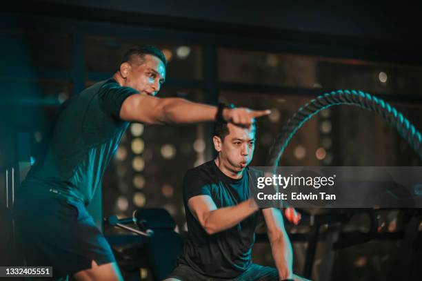 asian indian personal trainer encouraging asian chinese mid adult man practicing challenging battle rope in gym - gym coach stock pictures, royalty-free photos & images