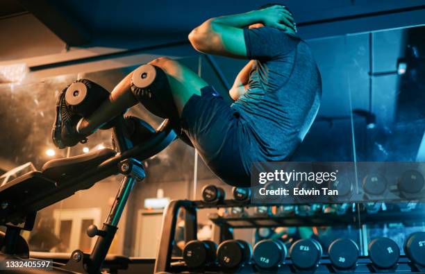 niedrige winkelansicht asiatischer indischer macho männlicher athlet sitzt -ups training im fitnessstudio in der nacht mit hantelbank - härte stock-fotos und bilder