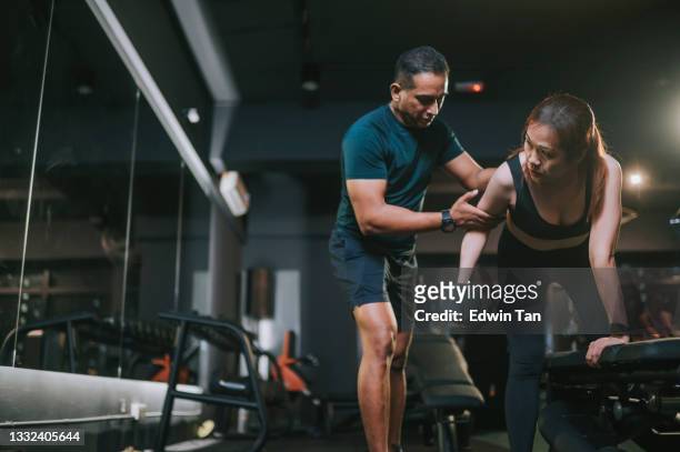 fitness instructor personal trainer guiding asian mid adult woman exercising with dumbbells in a lunge position at gym bench at night - fitness instructor at home stock pictures, royalty-free photos & images