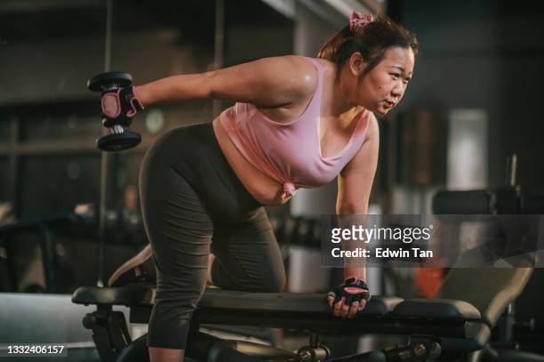 cuerpo positivo mujer adulta media asiática haciendo ejercicio con mancuernas en una posición de estocada en el banco del gimnasio por la noche - complexión gruesa fotografías e imágenes de stock
