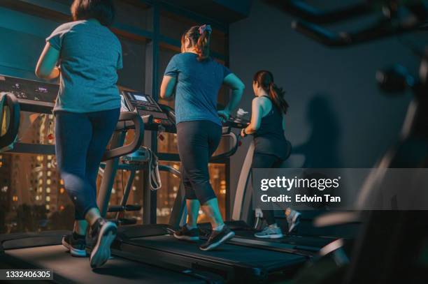 bajo ángulo de visión trasera cuerpo positivo mujer corriendo cinta de correr junto con su amiga en el gimnasio en la noche frente a la luz de la calle de la ciudad - female muscular calves fotografías e imágenes de stock