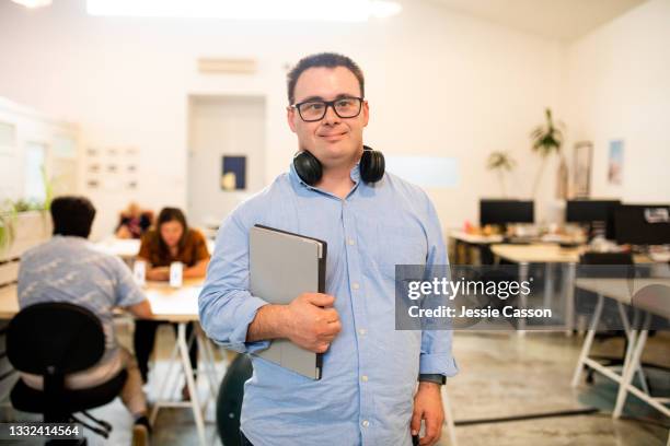 a man with down syndrome standing in a co-working space with his laptop - new zealand business stock pictures, royalty-free photos & images