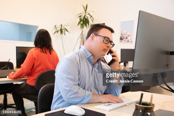 man with down syndrome on phone in a co working office - down's syndrome fotografías e imágenes de stock