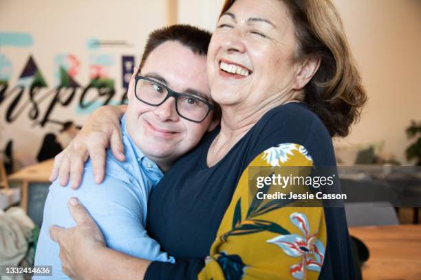 an adult man with down syndrome hugs his mum - workplace relations stock pictures, royalty-free photos & images