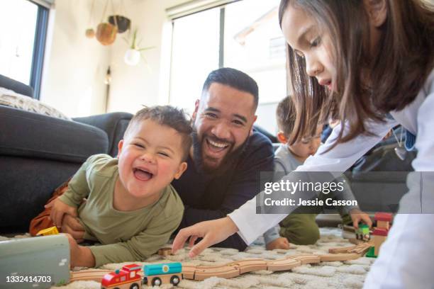father and children play with wooden train set - one clild has down syndrome - habitant-des-îles-du-pacifique photos et images de collection