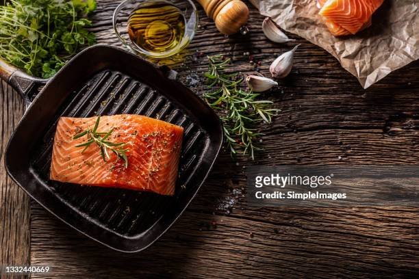 raw salmon steak in grill pan, salt, pepper, rosemary, olive oil and garlic on rustic oak table. - salmon stock pictures, royalty-free photos & images