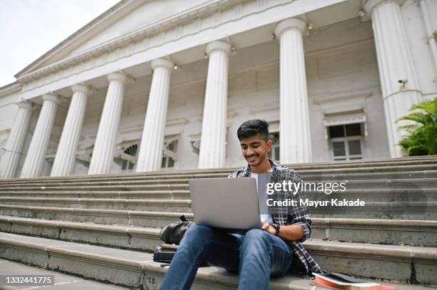 university student sitting outside on steps and using laptop - indian college students stock-fotos und bilder