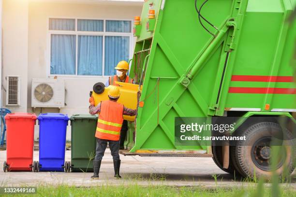 two dustmen standing by a dustbin lorry emptying wheelie bins, thailand - dustbin lorry stock pictures, royalty-free photos & images