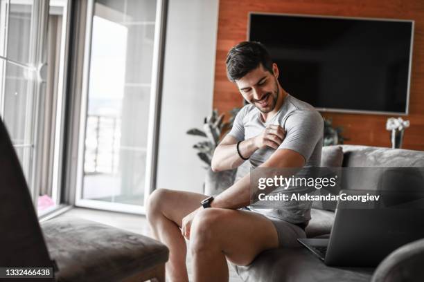 lächelnder mann genießt neues unterwäsche-t-shirt zu hause, während er laptop auf dem sofa benutzt - get dressed male stock-fotos und bilder