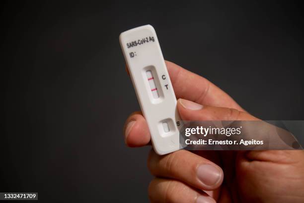 male hand holding a positive sars-covid test against dark background - teste de diagnóstico rápido - fotografias e filmes do acervo