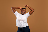 Portrait of casual young black woman dancing, brown wall