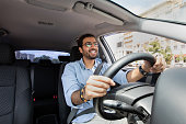 Joyful middle-eastern man driving car, shot from front pannel