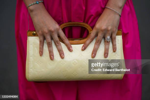Gabriella Berdugo wears a Fuchsia neon pink dress, finger rings, a vintage vinyl beige long bag with embossed monograms from Louis Vuitton, on August...