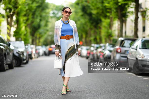 Gabriella Berdugo wears Loewe sunglasses, a golden large maxi chain necklace, a blue top, a long shirt with colored printed landscape details from...