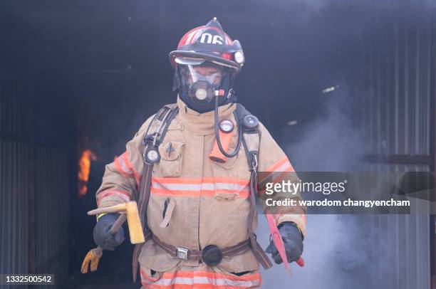 firefighter wearing protective workwear holding axe. - firefighter uniform stock pictures, royalty-free photos & images