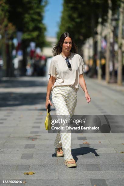 Alice Barbier wears black sunglasses, gold chain necklaces, a beige t-shirt, beige and pale green checkered large pants, a yellow Reedition 2000...