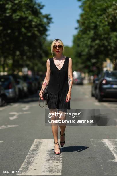 Emy venturini wears black sunglasses, gold large earrings, a long gold chain necklace, a black V-neck / tank-top / buttoned / short ribbed dress, a...