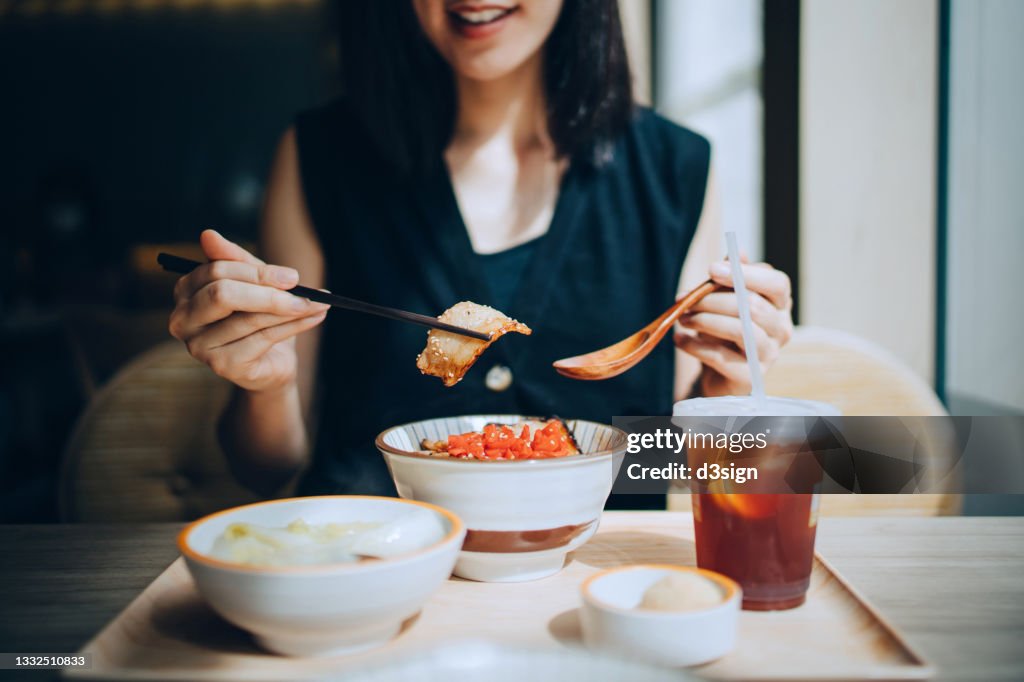 Close up of smiling young Asian woman enjoying freshly served traditional Japanese Yakiniku pork rice bowl with side dishes in restaurant. Asian cuisine and food culture. Eating out lifestyle
