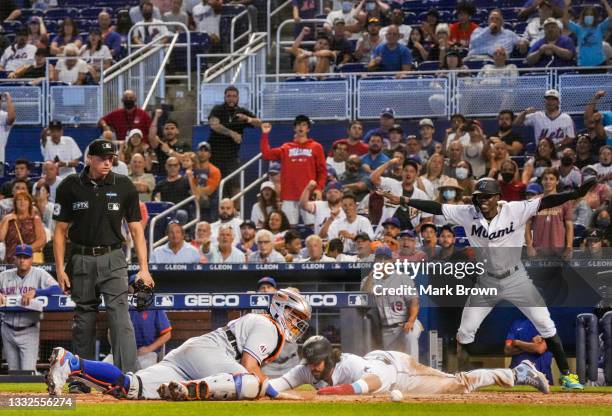 Jorge Alfaro of the Miami Marlins slides home to score while Jazz Chisholm Jr. #2 signals safe, as Tomás Nido of the New York Mets can not maintain...