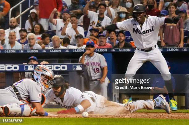 Jorge Alfaro of the Miami Marlins slides into home plate for the run while Jazz Chisholm Jr. #2 signals safe, as Tomás Nido of the New York Mets can...