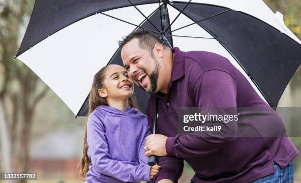 hispanic girl talking to father under umbrella in park - under value stock pictures, royalty-free photos & images