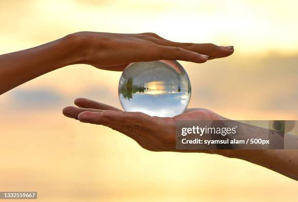 cropped hand holding crystal ball against sky during sunset,wara,sulawesi selatan,indonesia - better world stockfoto's en -beelden