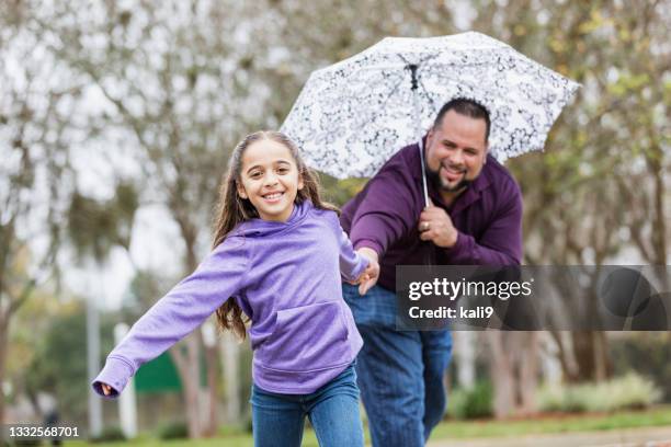 hispanic girl pulling father's hand, playing in the rain - guy girl street laugh stock pictures, royalty-free photos & images