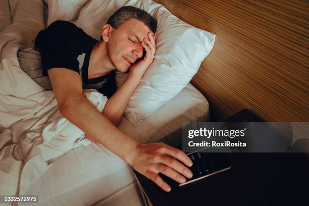 adult man asleep turning off his cell phone alarm - alarm clock stock-fotos und bilder