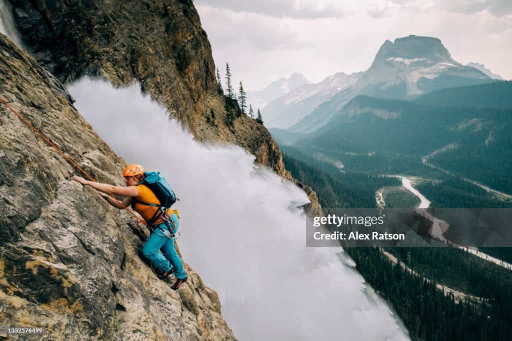 Female Rock climber climbs beside dramatic waterfall in Yoho National Park