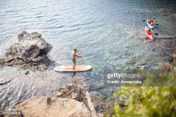 paddleboarder and kayakers off mediterranean coastline - rocky coastline stock pictures, royalty-free photos & images
