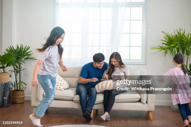 while active kids running parents resting on sofa using laptop - hot wife stockfoto's en -beelden