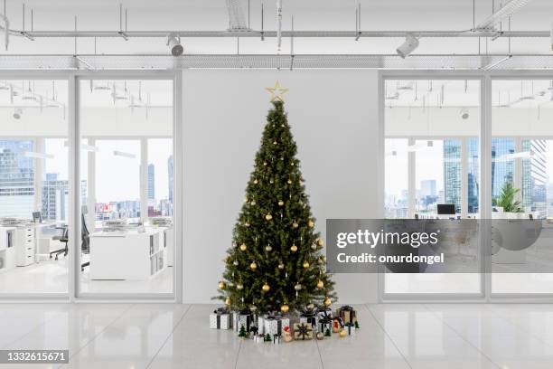 christmas tree with ornaments and gift boxes in front of white blank wall in open plan office with cityscape background - christmas office party stock pictures, royalty-free photos & images