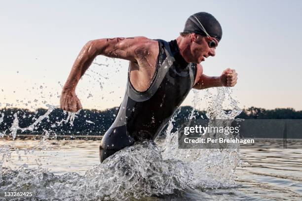 a male triathlete running out of the water - schwimmen wettkampf stock-fotos und bilder