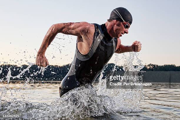 a male triathlete running out of the water - natación fotografías e imágenes de stock