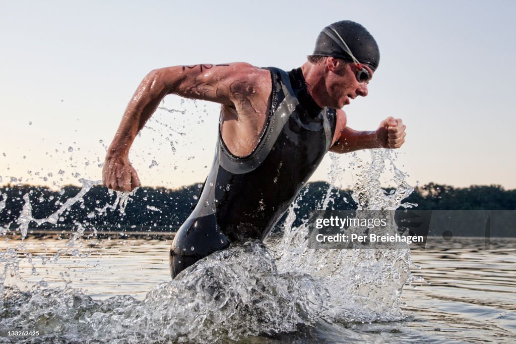 A male triathlete running out of the water