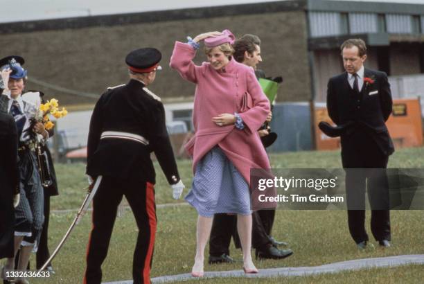 British Royal Diana, Princess of Wales , wearing a pink coat with a matching pink hat, and a blue-and-white polka dot dress, holding onto her hat as...