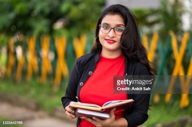 young female student reading book or document outdoor - rode rok stockfoto's en -beelden